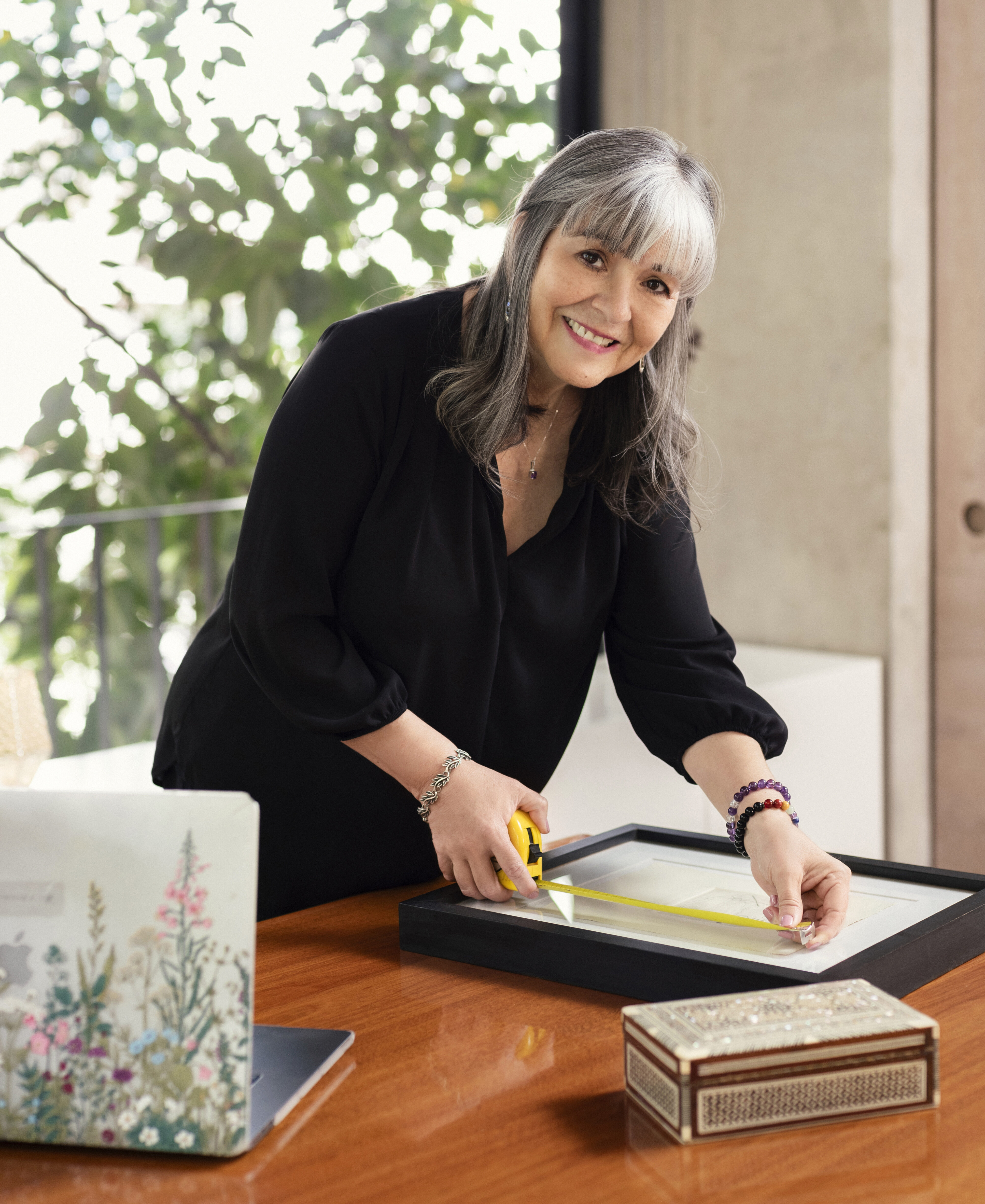 Analee McClellan, Acanthus Appraisals and Consultation Services Principal, measuring a framed artwork on a wooden table with other decorative items