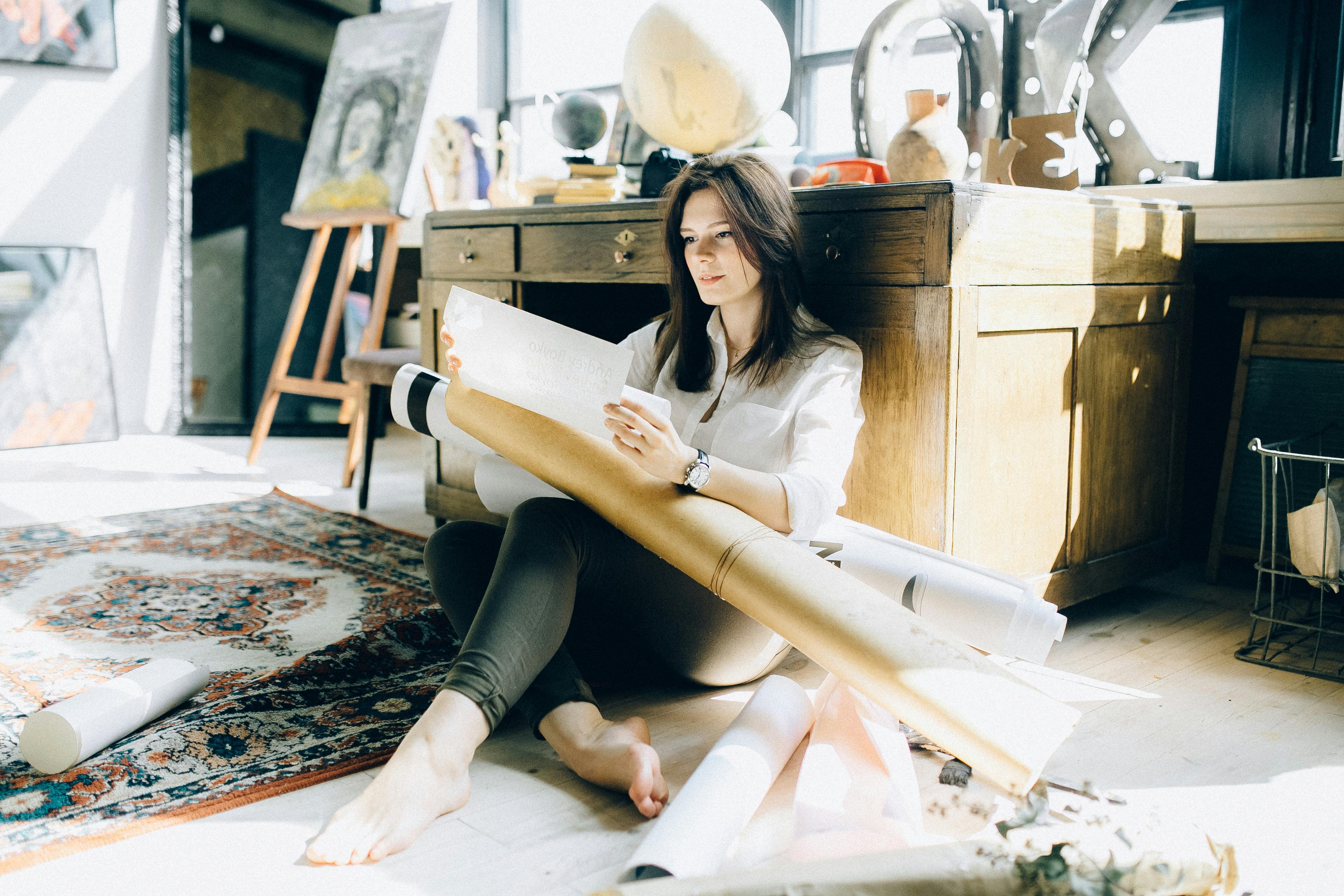 Woman sitting on the floor reading a document with rolled up posters on her lap