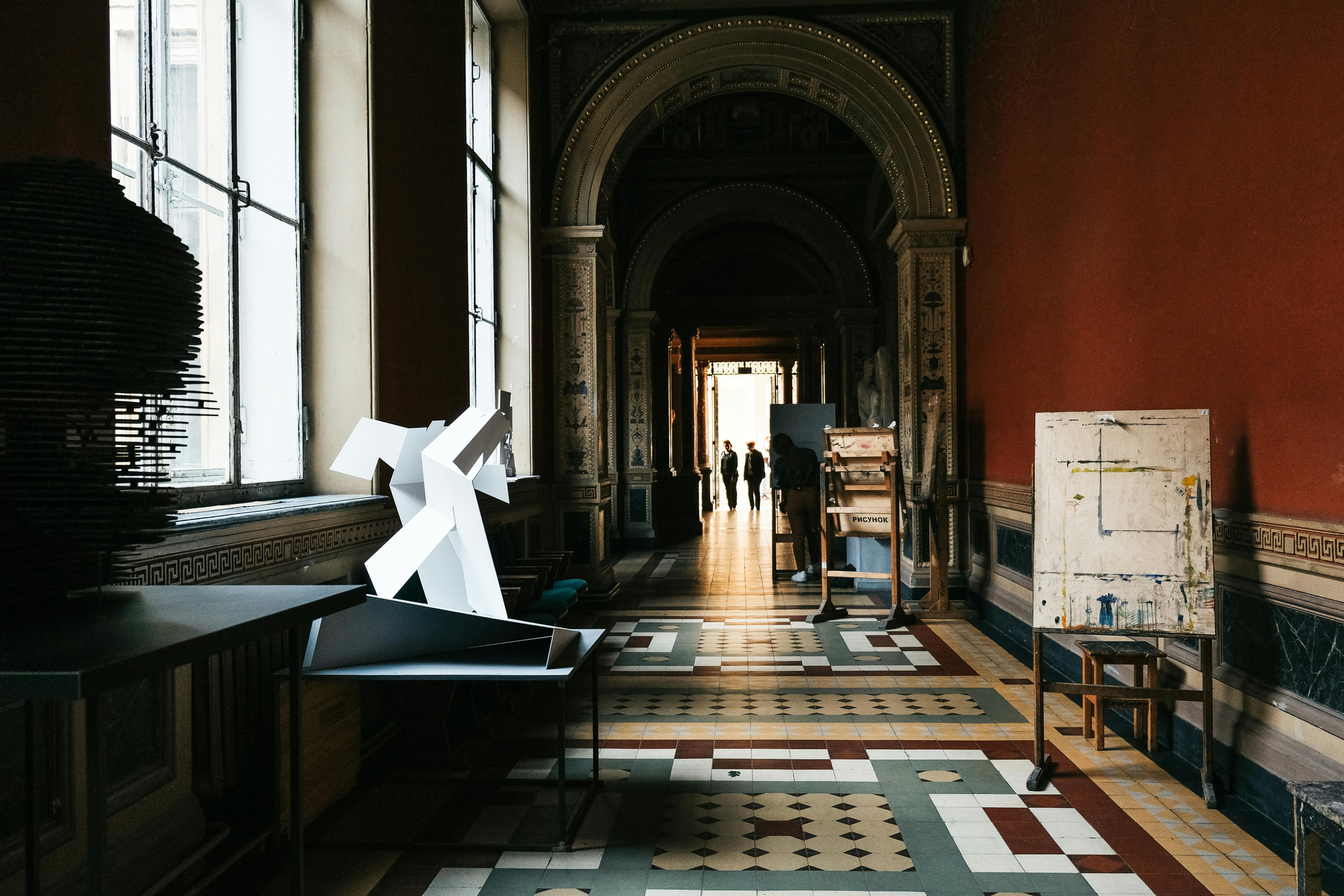 Sculptures and paintings in a grand hallway with a carved arch and colorful floor